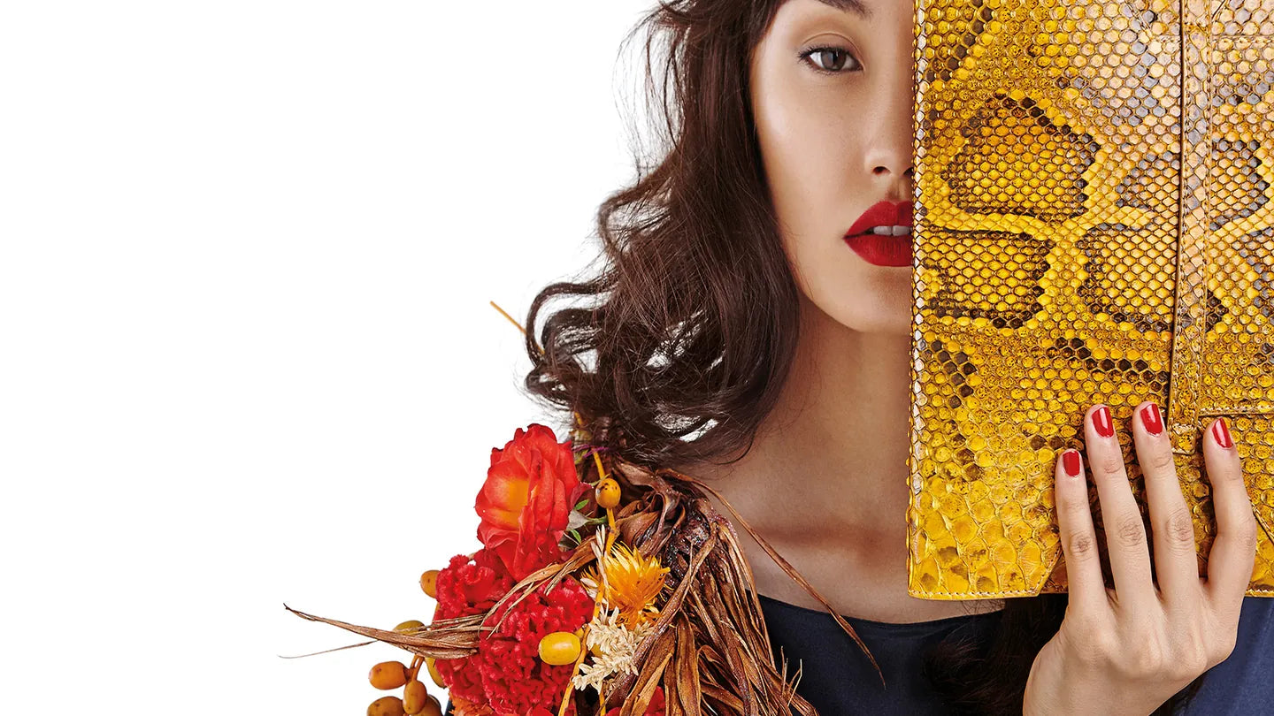 Model holding a yellow python-leather Kat van Duinen clutch over half her face, with a bouquet of red and dried flowers at her shoulder