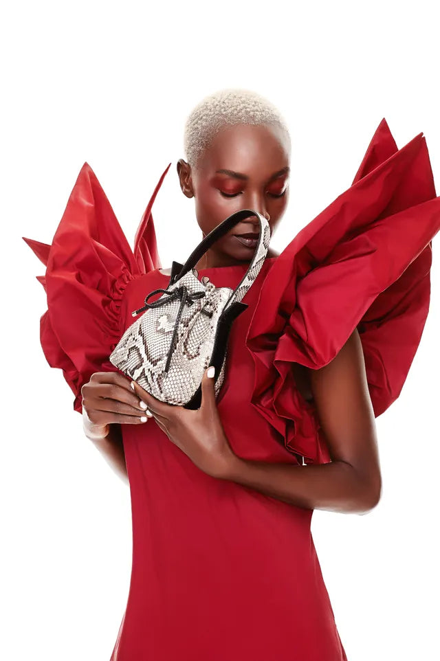 Model in a red ruffled gown holding a small natural python-leather bucket bag
