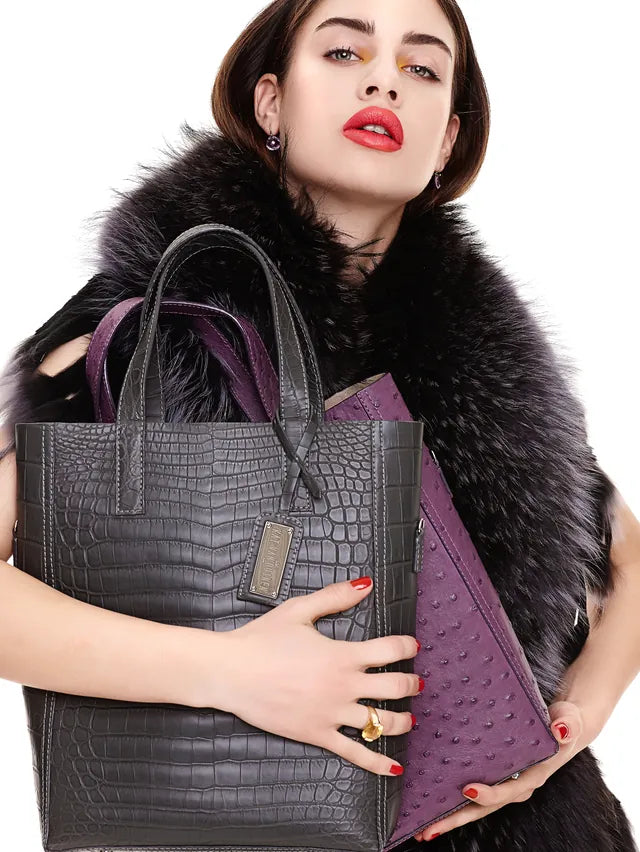 Model in a black fur stole carrying a charcoal crocodile-embossed tote and a purple ostrich-leather clutch